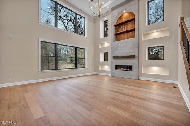 2705 Rocky Ridge Dr, Westlake, OH 44145 - unfurnished living room featuring a high ceiling, built in shelves, light wood-style floors, a fireplace, and a chandelier