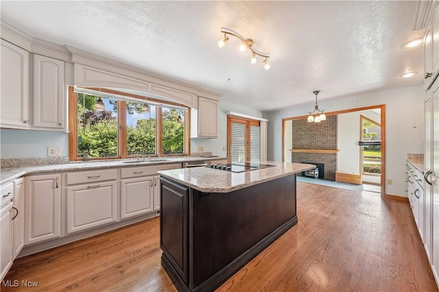 118 Steeplechase Ln, Munroe Falls, OH 44262 - kitchen with light wood finished floors, a fireplace, black electric stovetop, a kitchen island, and pendant lighting