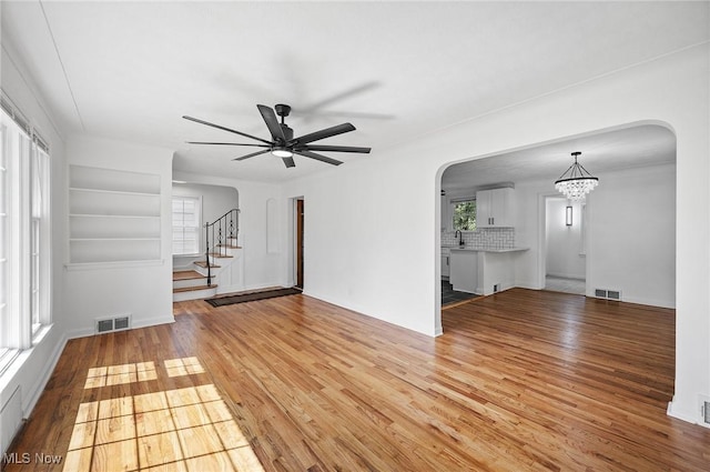 3722 Avalon Rd, Shaker Heights, OH 44120 - unfurnished living room with light wood-type flooring, arched walkways, a ceiling fan, and a chandelier
