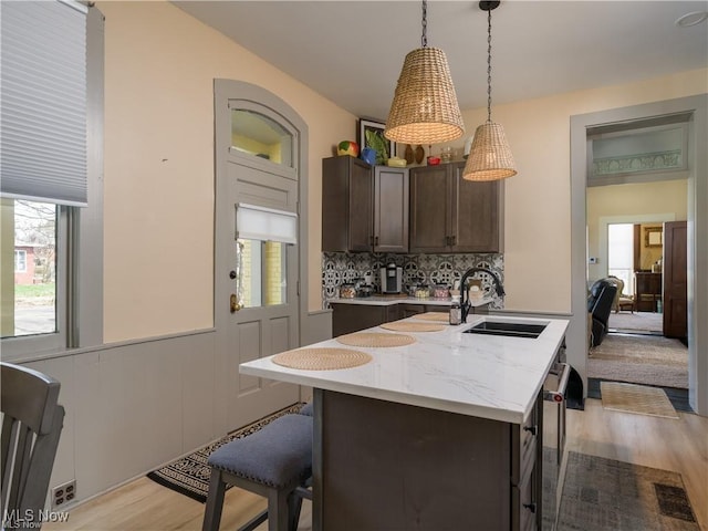 203 W 6th St, Dover, OH 44622 - kitchen with light wood-style floors, a center island with sink, a breakfast bar, pendant lighting, and a wainscoted wall