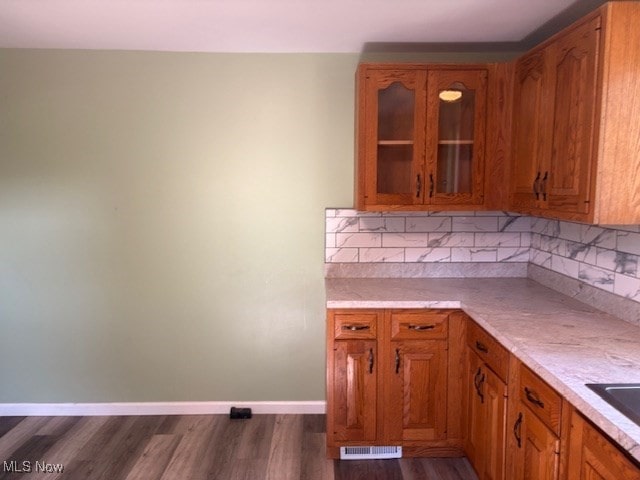 15920 Grove St, Middlefield, OH 44062 - kitchen featuring brown cabinets, dark wood-style floors, glass insert cabinets, light countertops, and decorative backsplash