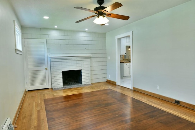 400 Spring St, Struthers, OH 44471 - unfurnished living room with light wood finished floors, a ceiling fan, baseboard heating, a brick fireplace, and recessed lighting