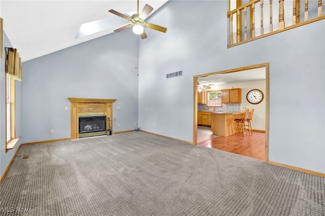 1550 Rebel St SW, Canton, OH 44706 - unfurnished living room featuring light carpet, a ceiling fan, high vaulted ceiling, a glass covered fireplace, and a skylight