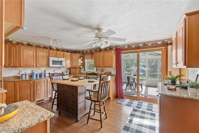 578 25th St NW, Massillon, OH 44647 - kitchen with white microwave, a breakfast bar, a ceiling fan, wood finished floors, and a textured ceiling