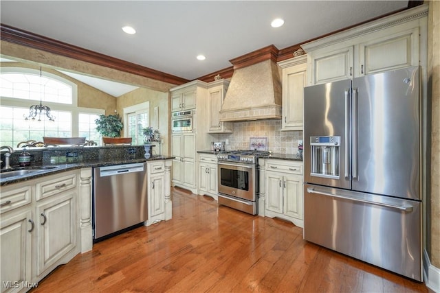 8309 Gentry St NW, Massillon, OH 44646 - kitchen featuring stainless steel appliances, custom range hood, vaulted ceiling, cream cabinets, and light wood finished floors