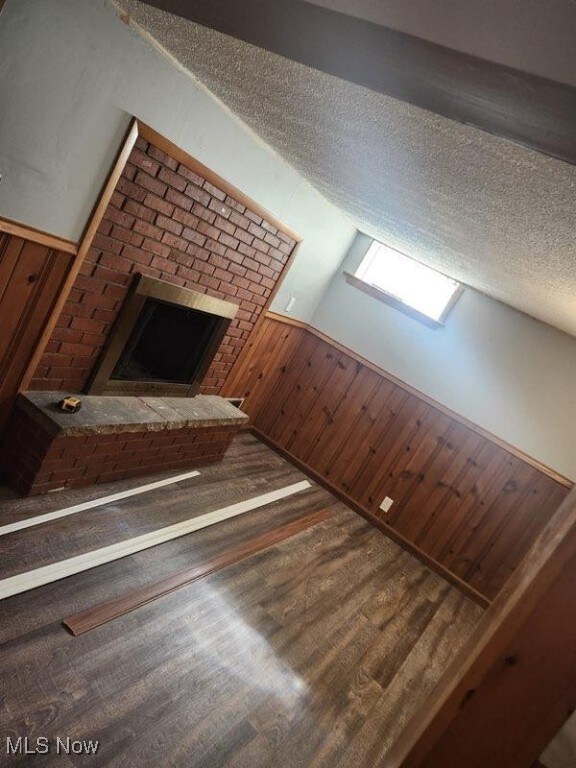 1146 Easton Dr, Akron, OH 44310 - unfurnished living room with a brick fireplace, wood finished floors, wooden walls, a textured ceiling, and a wainscoted wall