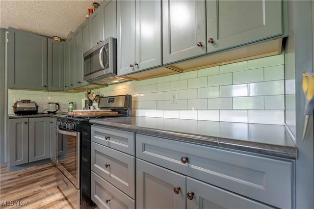 2176 Pageant Rd SE, Carrollton, OH 44615 - kitchen featuring stainless steel appliances, a textured ceiling, dark countertops, decorative backsplash, and light wood-style floors