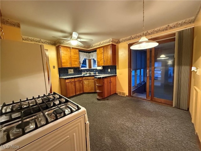 kitchen featuring white appliances, brown cabinetry, a ceiling fan, dark carpet, and tasteful backsplash