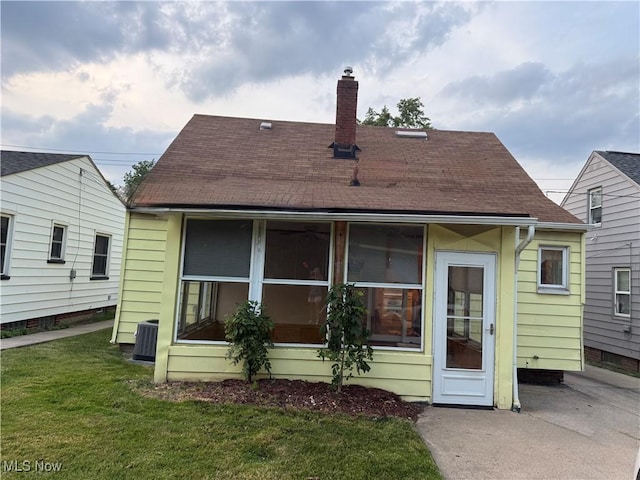 back of property with a chimney, roof with shingles, and a yard