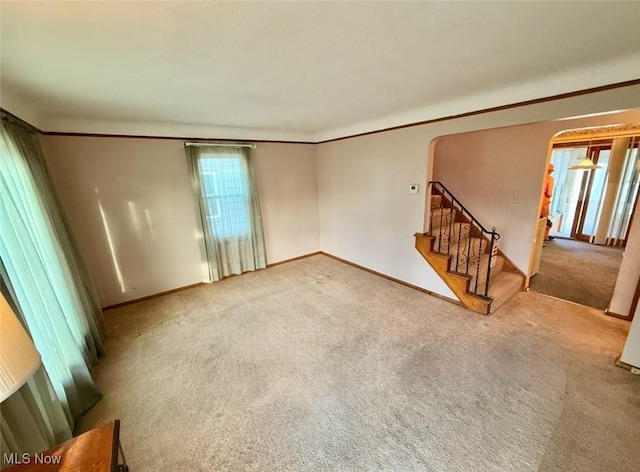 unfurnished living room with arched walkways, carpet floors, and stairway