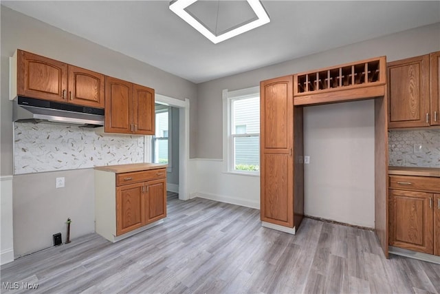 18104 Garden Blvd, Warrensville Heights, OH 44128 - kitchen with under cabinet range hood, light wood-style flooring, brown cabinetry, decorative backsplash, and light countertops