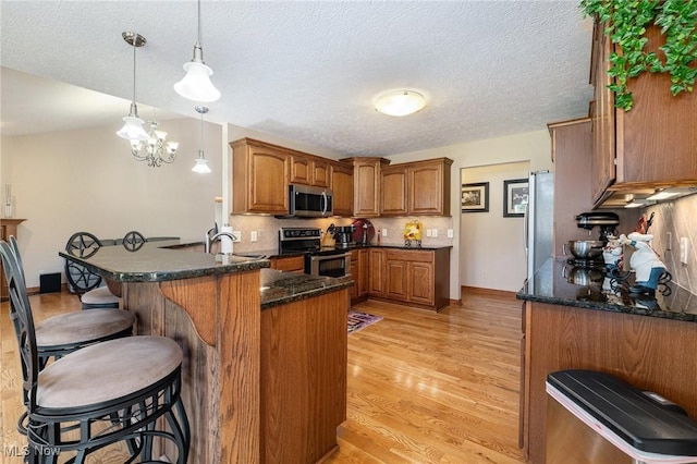 6782 Fawndale Dr, Medina, OH 44256 - kitchen featuring appliances with stainless steel finishes, a peninsula, brown cabinetry, a breakfast bar area, and light wood-style floors