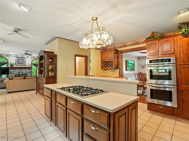 2526 Ashbrook Dr, Ashtabula, OH 44004 - kitchen featuring appliances with stainless steel finishes, light tile patterned floors, a ceiling fan, a fireplace, and brown cabinets