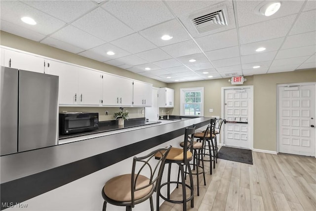 2021 King James Pkwy Unit 228, Westlake, OH 44145 - kitchen featuring black microwave, freestanding refrigerator, light wood-type flooring, white cabinets, and a breakfast bar