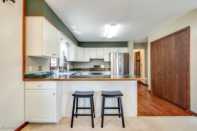 3613 Peninsula Dr, Akron, OH 44319 - kitchen with stainless steel appliances, under cabinet range hood, a peninsula, white cabinetry, and a kitchen breakfast bar