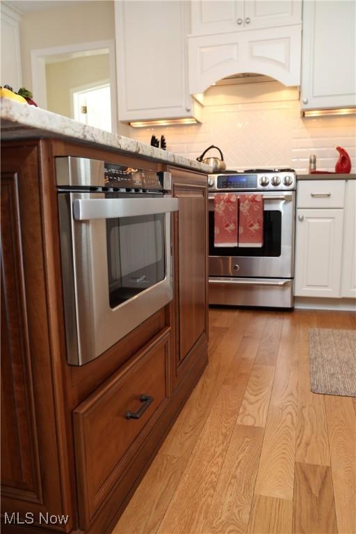 31382 Saint Andrews, Westlake, OH 44145 - kitchen featuring stainless steel appliances, custom range hood, light wood-style floors, white cabinetry, and decorative backsplash