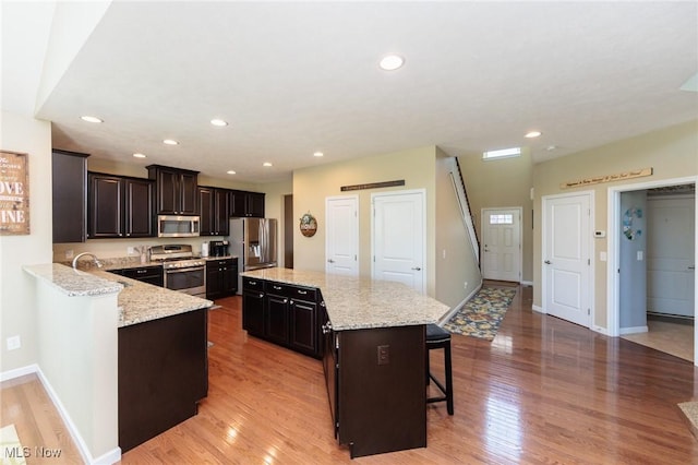 3139 Junior Pkwy, Brunswick, OH 44212 - kitchen with appliances with stainless steel finishes, a breakfast bar, light wood finished floors, a kitchen island, and light stone countertops
