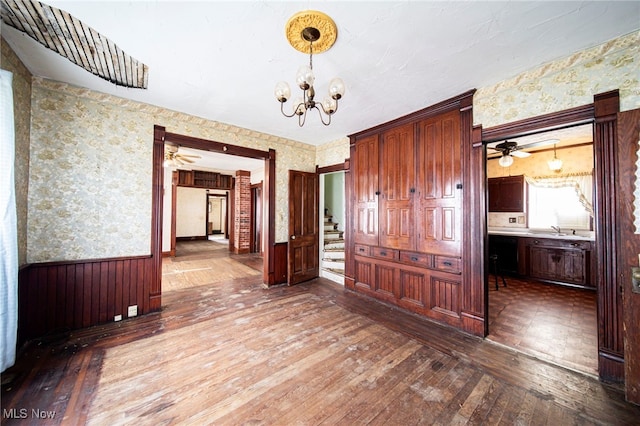 238 Whitney St, Conneaut, OH 44030 - unfurnished dining area featuring wallpapered walls, a wainscoted wall, hardwood / wood-style floors, a chandelier, and a ceiling fan