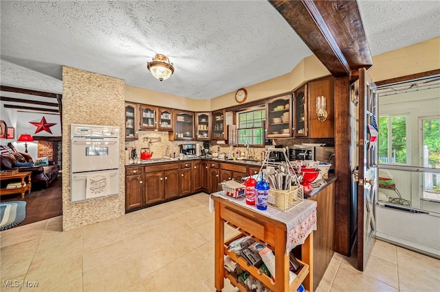 278 Rosewae Ave, Cortland, OH 44410 - kitchen with a textured ceiling, decorative backsplash, glass insert cabinets, light tile patterned floors, and double oven