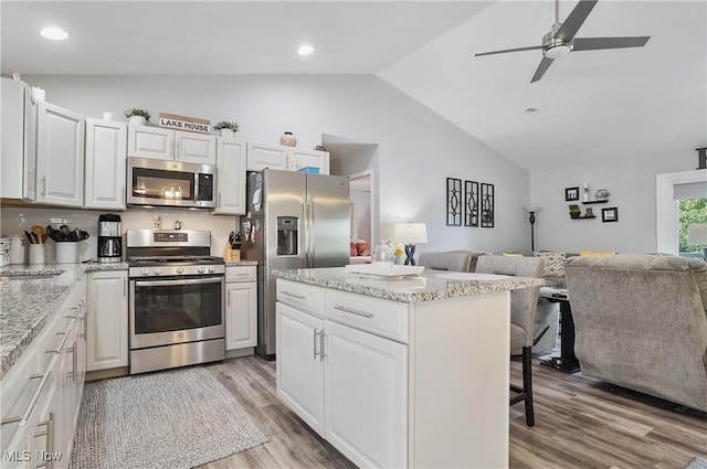 47688 Tomahawk Dr, Negley, OH 44441 - kitchen featuring appliances with stainless steel finishes, open floor plan, vaulted ceiling, light wood finished floors, and a kitchen bar