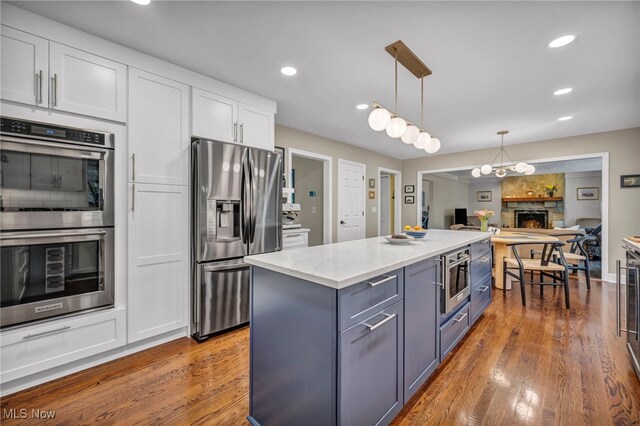 561 Willard Rd, Aurora, OH 44202 - kitchen with appliances with stainless steel finishes, white cabinetry, wood finished floors, hanging light fixtures, and a center island