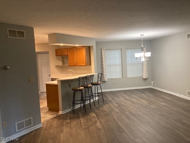 205 S Aspen Unit 4, Warren, OH 44484 - kitchen with a breakfast bar, brown cabinetry, a chandelier, dark wood finished floors, and light countertops
