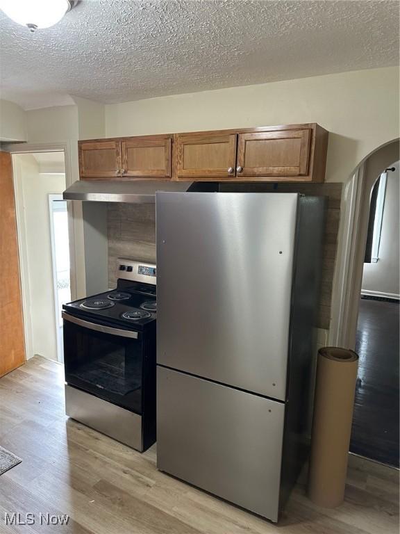 1042 Frederick Blvd, Akron, OH 44320 - kitchen with appliances with stainless steel finishes, under cabinet range hood, arched walkways, light wood-type flooring, and brown cabinetry