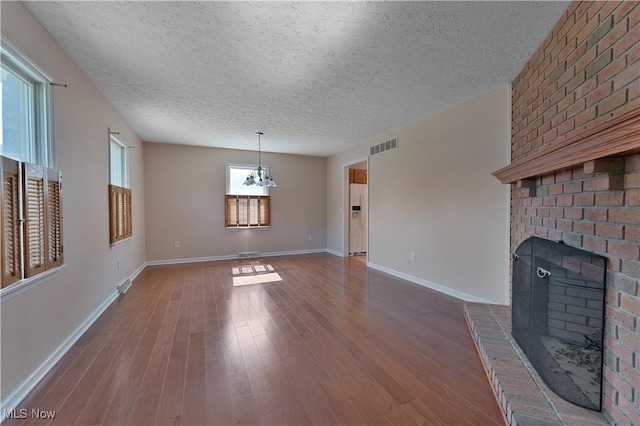 233 Robbies Run, Cortland, OH 44410 - unfurnished living room featuring a textured ceiling, a brick fireplace, wood finished floors, and a chandelier