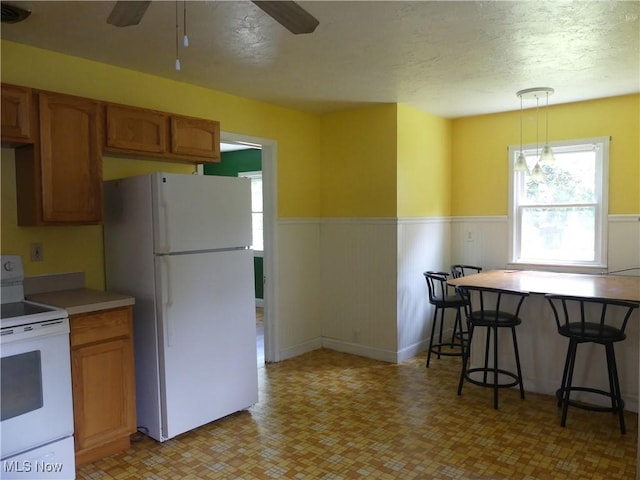 6069 Hyde St, Mentor, OH 44060 - kitchen featuring white appliances, a ceiling fan, wainscoting, brown cabinetry, and a textured ceiling