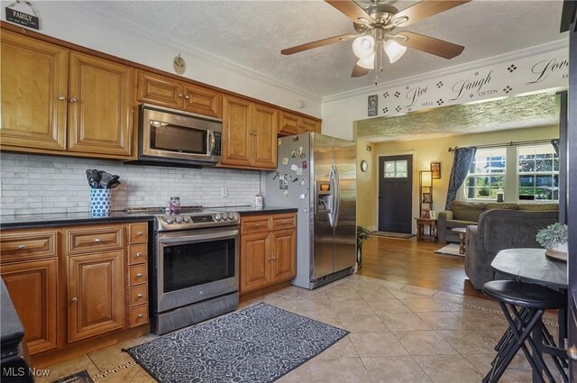 13774 Smith Goshen Rd, Beloit, OH 44609 - kitchen featuring appliances with stainless steel finishes, brown cabinets, dark countertops, ornamental molding, and a ceiling fan