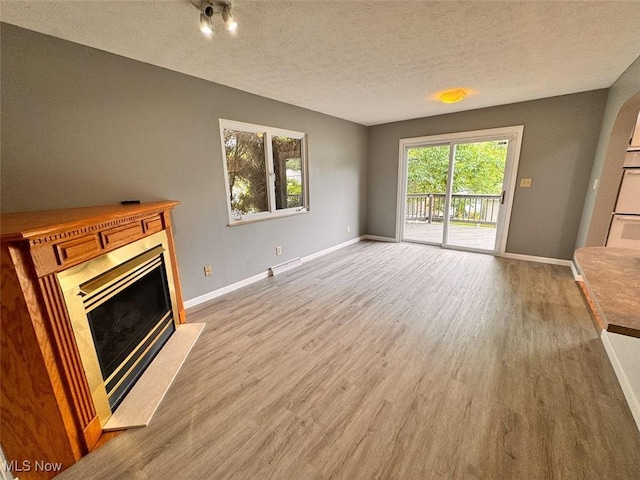 1587 Hilda St, Lakemore, OH 44250 - unfurnished living room featuring a fireplace with raised hearth, light wood-style flooring, and a textured ceiling
