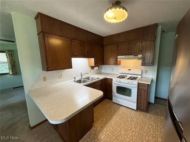 122 N Fairview Ave, Dover, OH 44622 - kitchen with white gas range, under cabinet range hood, freestanding refrigerator, light countertops, and a peninsula