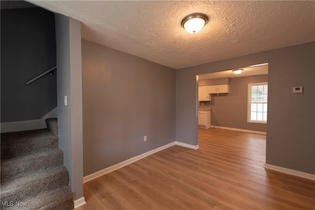 1022 Big Falls Ave, Akron, OH 44310 - unfurnished living room with a textured ceiling, light wood-style floors, and stairs