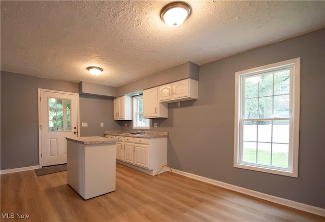 1022 Big Falls Ave, Akron, OH 44310 - kitchen with a textured ceiling, light wood-style flooring, white cabinets, a center island, and healthy amount of natural light