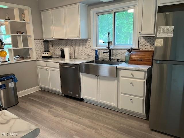 5559 Fitch Rd, North Olmsted, OH 44070 - kitchen featuring appliances with stainless steel finishes, white cabinets, light wood-style floors, and tasteful backsplash