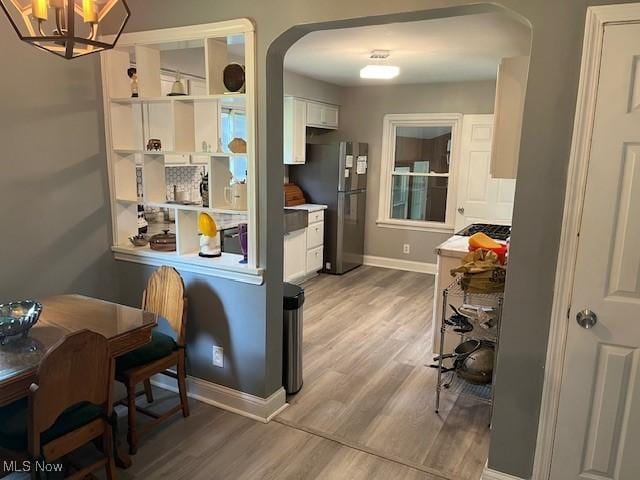 5559 Fitch Rd, North Olmsted, OH 44070 - kitchen with arched walkways, light wood-style flooring, freestanding refrigerator, white cabinetry, and a chandelier