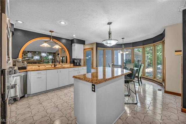 6869 Cliffside Dr, Vermilion, OH 44089 - kitchen with white cabinetry, a textured ceiling, a kitchen island, decorative light fixtures, and light stone countertops