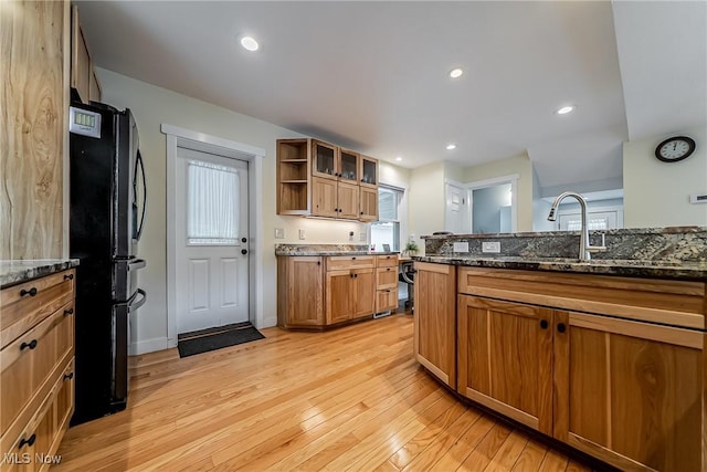 24690 Hawthorne Dr, Euclid, OH 44117 - kitchen featuring freestanding refrigerator, light wood-style flooring, dark stone counters, brown cabinetry, and glass insert cabinets