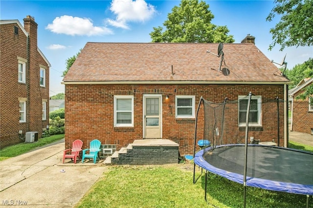 565 12th St, Campbell, OH 44405 - back of property with a trampoline, brick siding, a yard, a chimney, and a patio area