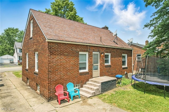 565 12th St, Campbell, OH 44405 - back of property featuring a trampoline, brick siding, a shingled roof, and a chimney