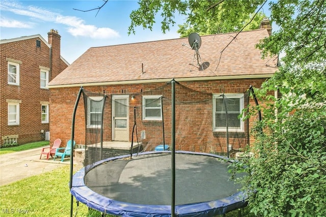 565 12th St, Campbell, OH 44405 - back of property featuring a trampoline, brick siding, a patio area, roof with shingles, and a yard