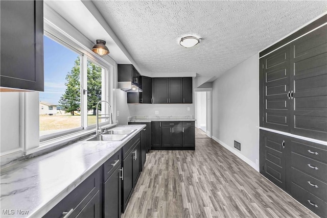 13050 Diagonal Rd, Salem, OH 44460 - kitchen with a textured ceiling, light wood-type flooring, light stone countertops, under cabinet range hood, and dark cabinetry