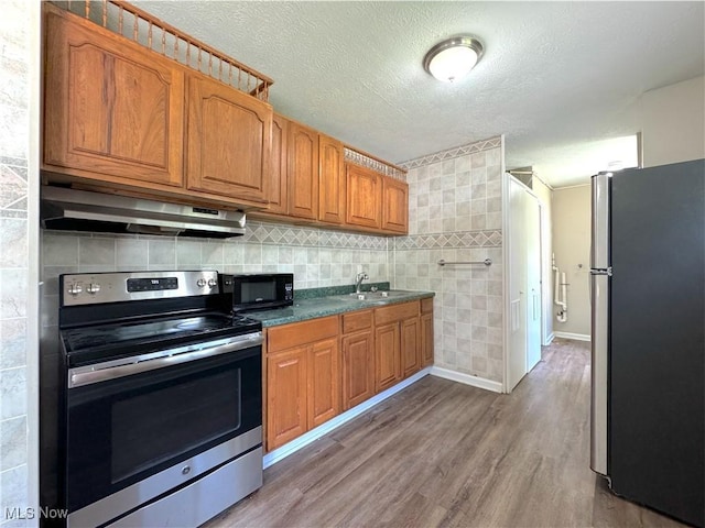 24525 Sherborne Rd, Bedford Heights, OH 44146 - kitchen featuring stainless steel appliances, under cabinet range hood, brown cabinetry, wood finished floors, and dark countertops
