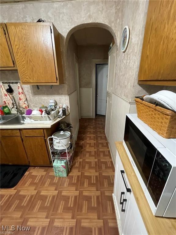 20520 Ball Ave, Euclid, OH 44123 - kitchen featuring white microwave, light countertops, arched walkways, and brown cabinetry