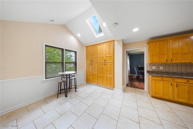 1141 Las Olas Blvd NW, North Canton, OH 44720 - kitchen featuring a skylight, vaulted ceiling, backsplash, light tile patterned flooring, and a wainscoted wall