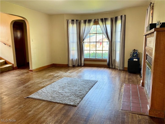1055 W Virginia Ave, Parkersburg, WV 26104 - unfurnished living room featuring wood finished floors, a fireplace with flush hearth, arched walkways, and stairs