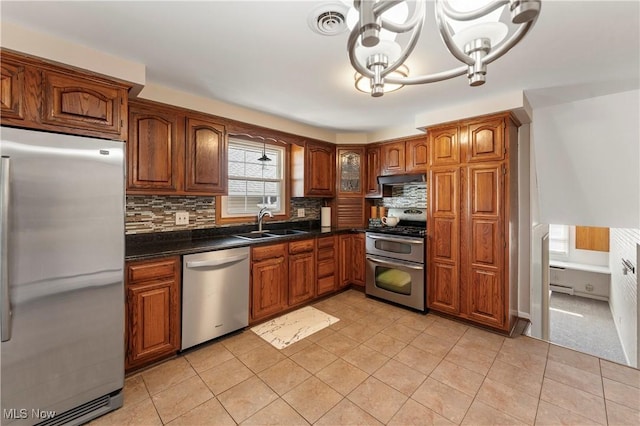 2615 Daffodil St NE, Canton, OH 44705 - kitchen with appliances with stainless steel finishes, brown cabinets, dark countertops, a chandelier, and light tile patterned flooring