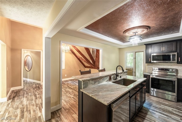 1915 Claus Rd, Vermilion, OH 44089 - kitchen with stainless steel appliances, a tray ceiling, wood finished floors, light stone counters, and a kitchen island with sink