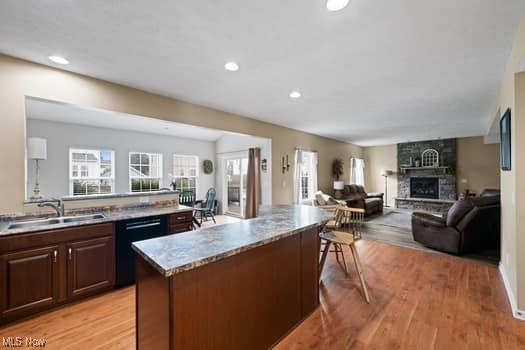 1932 Pinewood Ln, Painesville, OH 44077 - kitchen with black dishwasher, a fireplace, a kitchen bar, recessed lighting, and light wood-type flooring