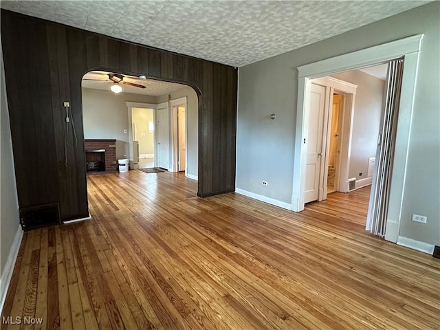 4011 E 29th St, Newburgh Heights, OH 44105 - empty room featuring arched walkways, wood-type flooring, a fireplace, wood walls, and ceiling fan